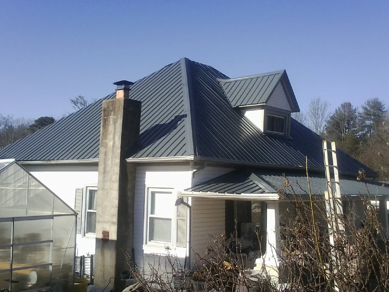 Dark blue standing seam metal roof on a white farmhouse with dormer — Slate & Tile Roof Repair by Roofing Brothers in Hickory Grove