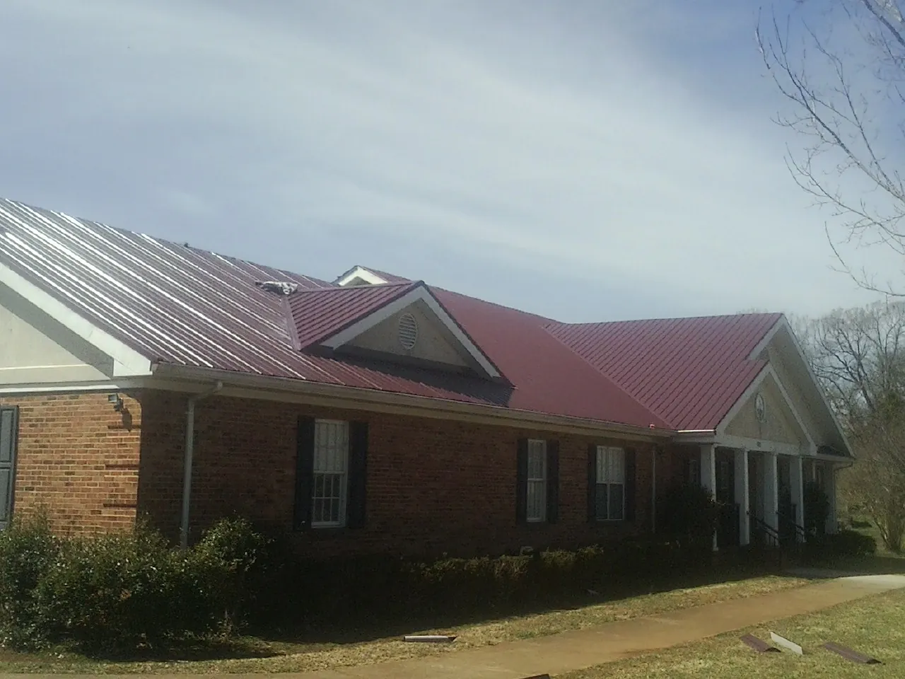 Red metal roof with gabled entries on a long brick building, from a Hail Damage Roof Repair job in Hickory Grove