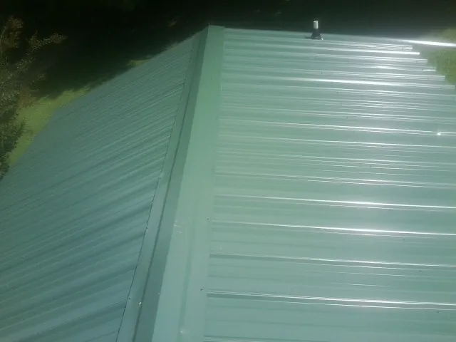 New green metal panels meeting at the ridge of a roof — Flat Roof Repair work by our crew in Hickory Grove