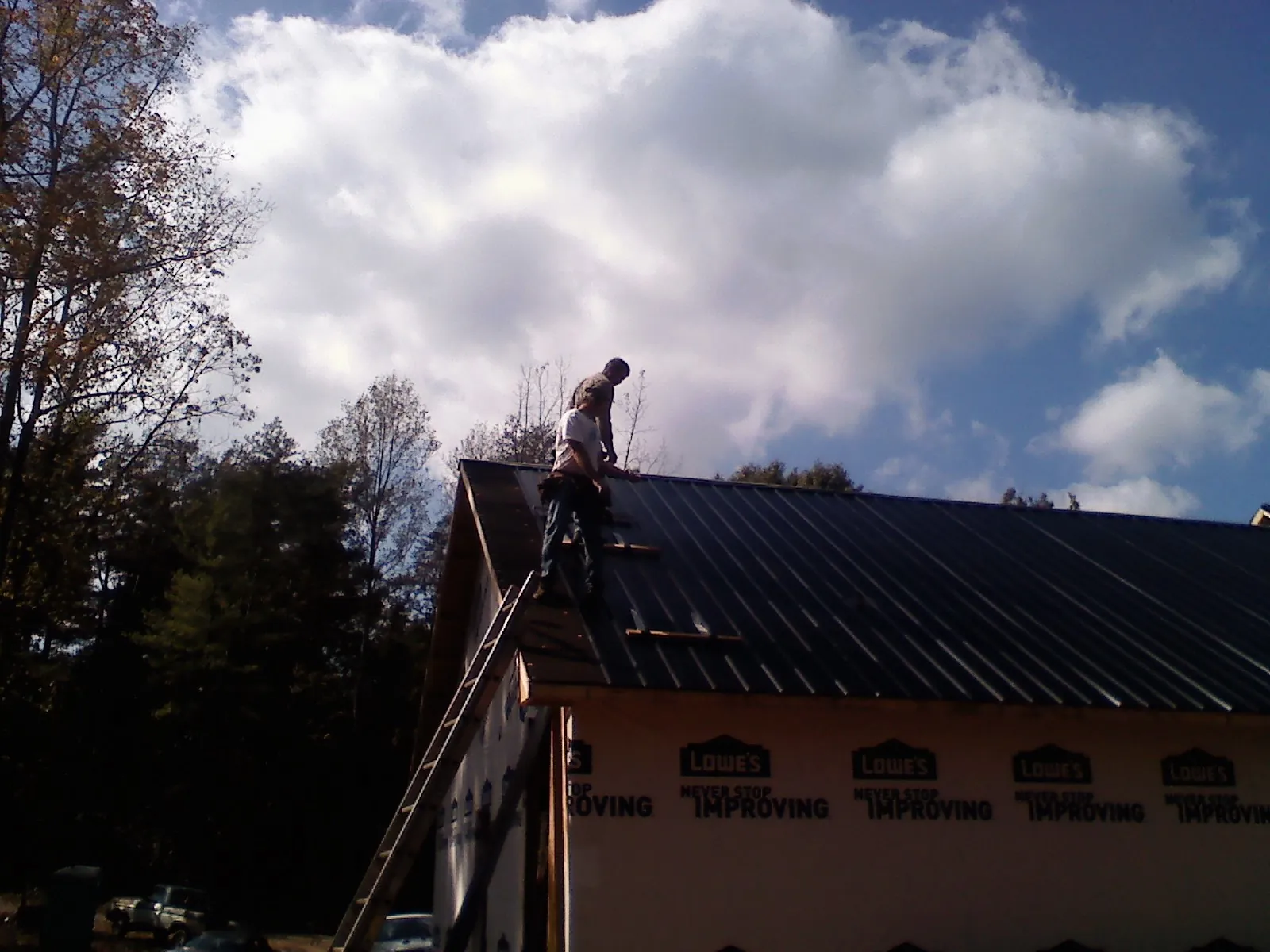Roofer fastening dark metal panels high against a cloudy sky, from a Roof Inspection job in Hickory Grove
