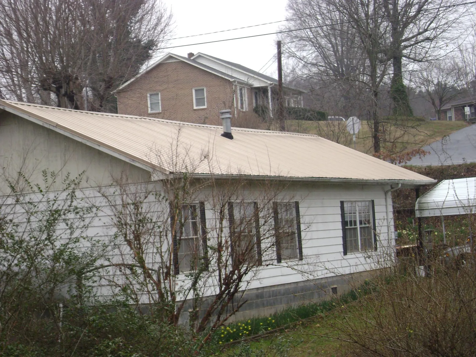 Tan metal roof on a white sided house set into a hillside — Commercial Roofing by Roofing Brothers in Hickory Grove
