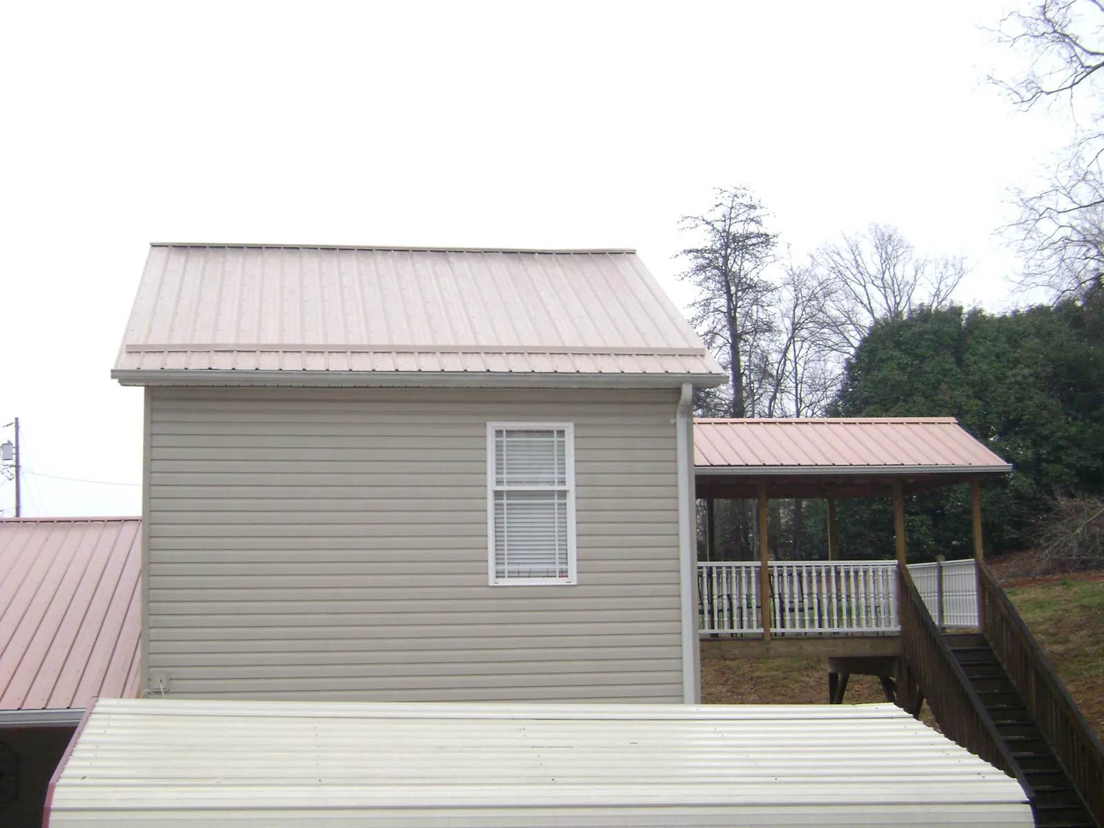 Tan metal roofs on a two story addition and attached porch, from a Roof Replacement job in Hickory Grove